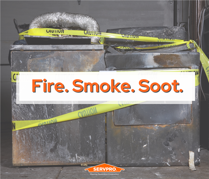 dryers covered in soot and caution tape, white text box with orange letters "soot fire smoke" SERVPRO logo bottom center
