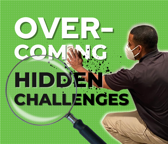 green background, SERVPRO technician in a mask wiping a wall, the text reads "overcoming hidden challenges," magnifying glass